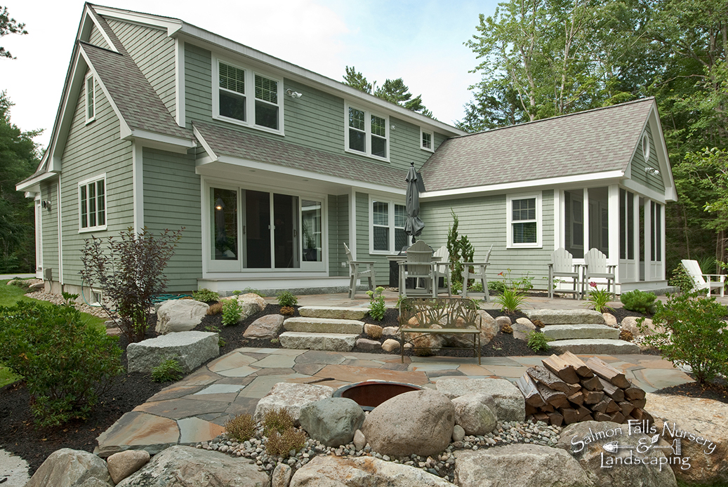 Bluestone patio with granite steps and a fieldstone fire pit behind a shingled home