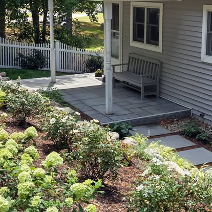 Garden beds and a stone patio beside a home